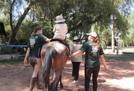 Volunteer Care A child rides a horse being led by volunteers on an Equine Therapy Project in Bolvia