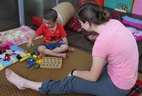 Volunteer Medicine & Healthcare A qualified Occupational Therapist volunteer in Vietnam assesses a disabled child using a game that requires fine motor skills.