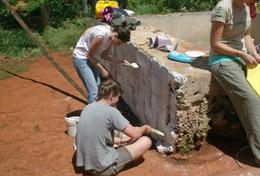 Volunteer Jamaica High School Special Building volunteers cover a brick wall with cement in a local community in Jamaica.