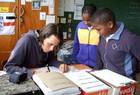 Volunteer South Africa Two school children watch as a Teaching volunteer demonstrates how to complete the English homework assigned to them.
